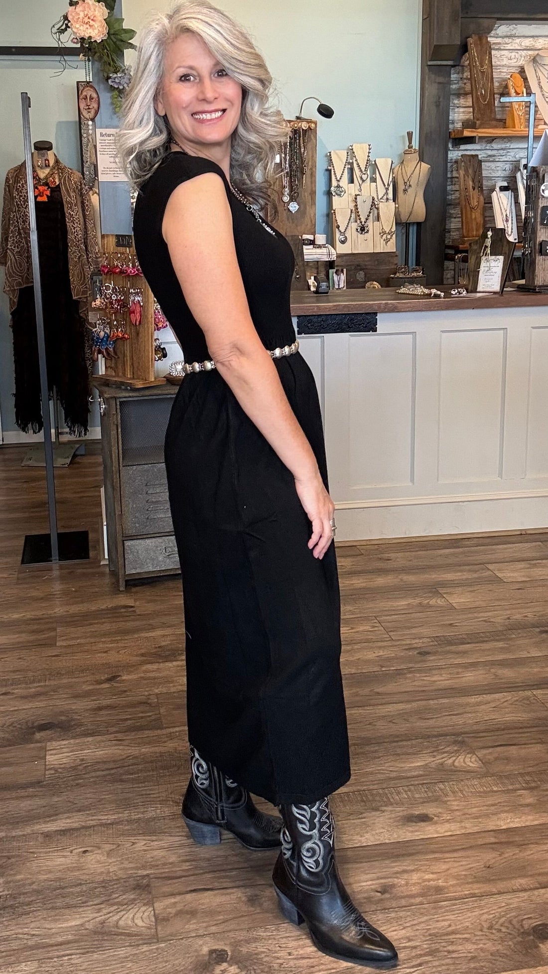 Woman in a black dress and cowboy boots standing in a store with mannequins and decor.
