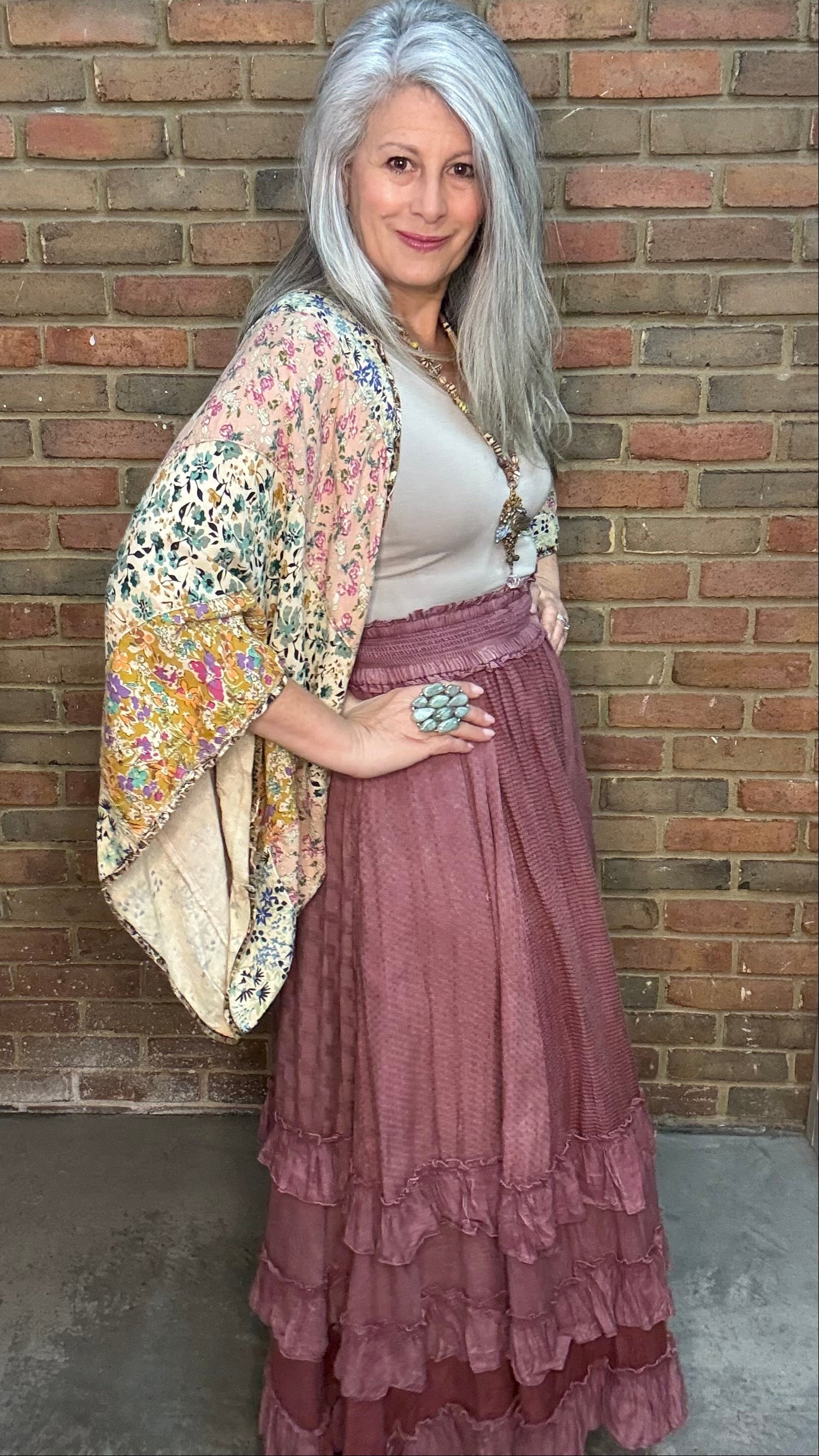 Woman wearing a Patchwork Kaftan Poncho and Rustic Textured Maxi Skirt against a brick wall.