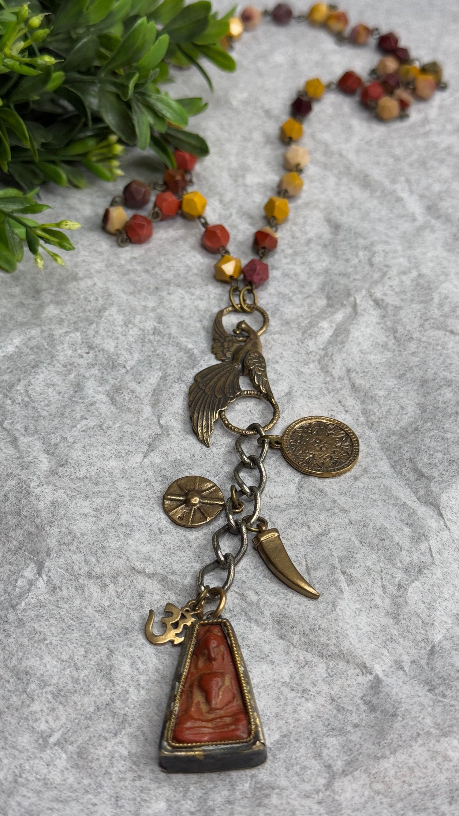 Necklace with various charms on a textured surface with greenery