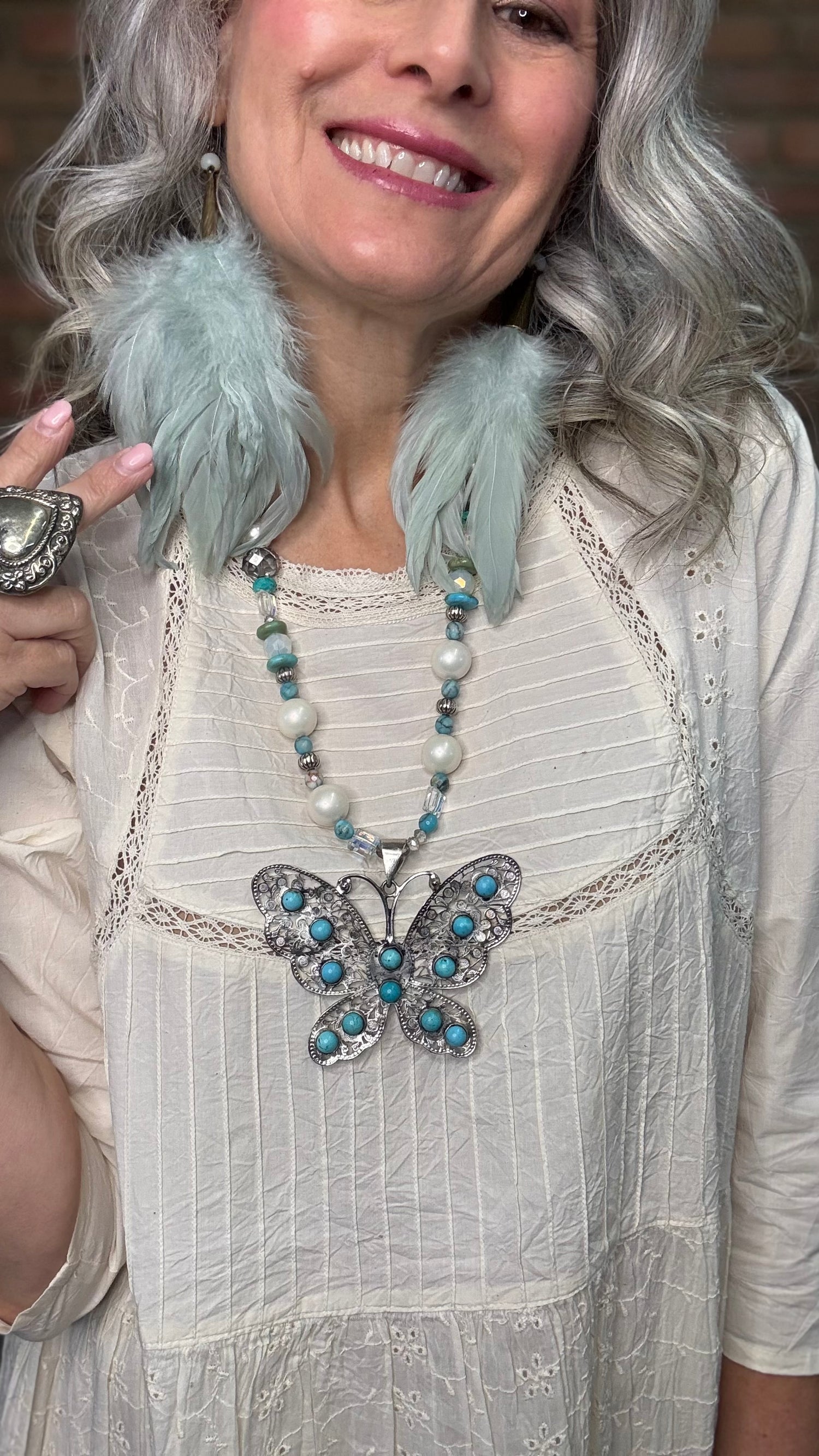 Woman wearing Silver Filigree Butterfly Necklace with turquoise stones and sage feather earrings.