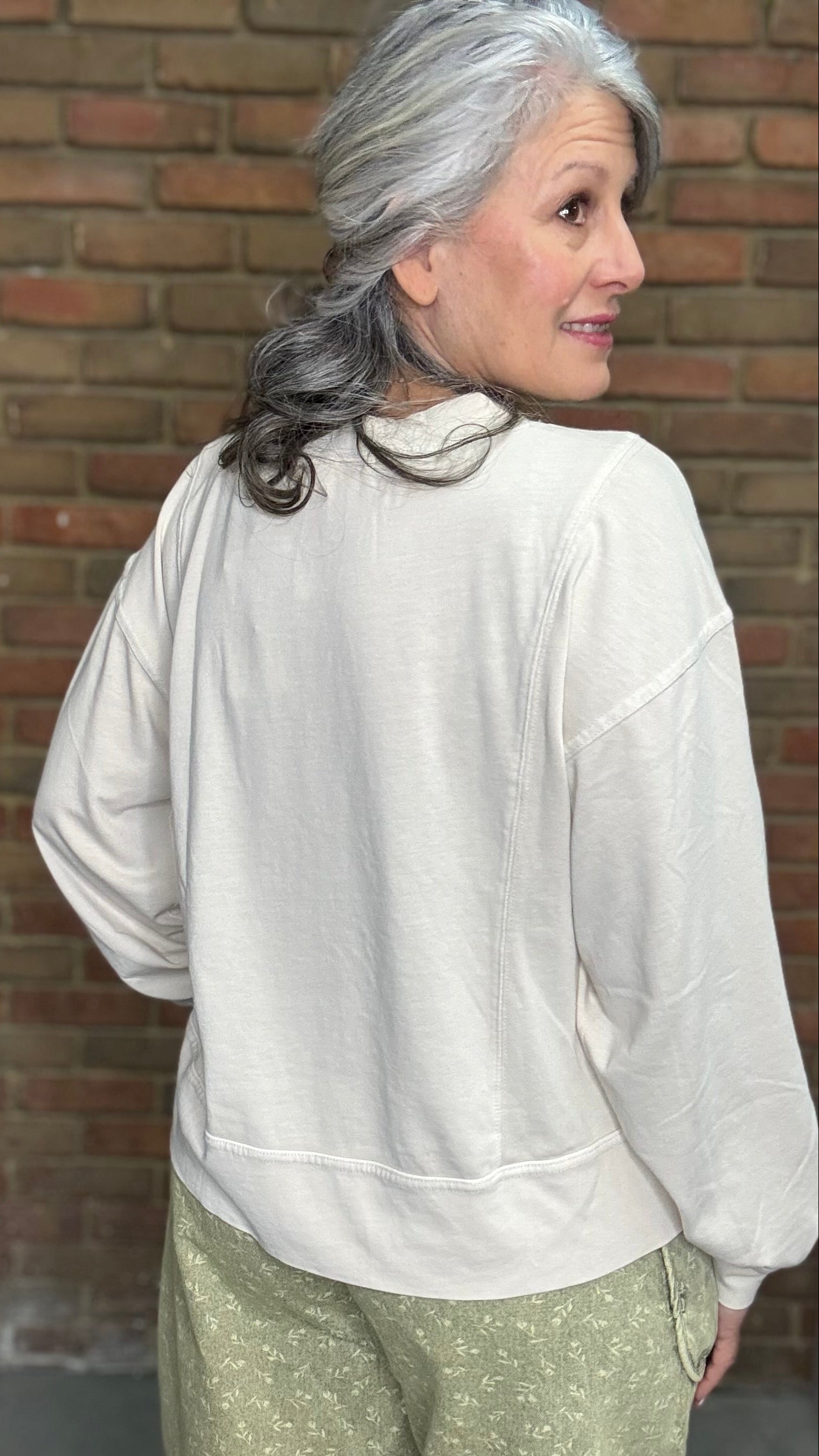 Woman standing against a brick wall wearing the Taupe Long Sleeve Top and Floral Printed Barrel Pants.