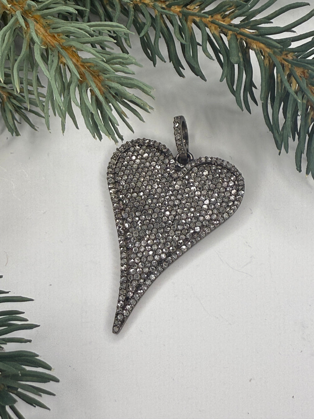 Heart-shaped pendant with pave diamonds on a light background with greenery
