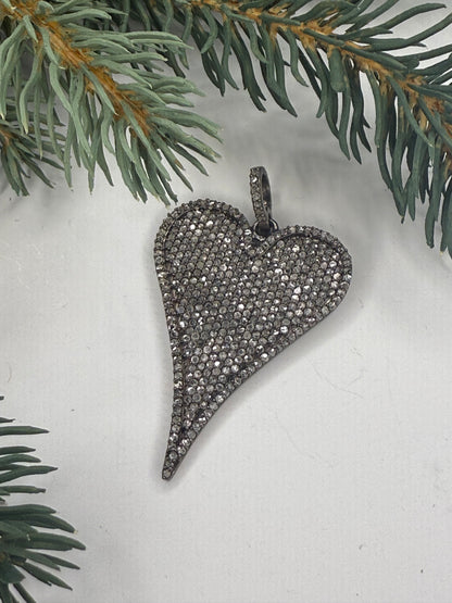 Heart-shaped pendant with pave diamonds on a light background with greenery