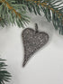 Heart-shaped pendant with pave diamonds on a light background with greenery
