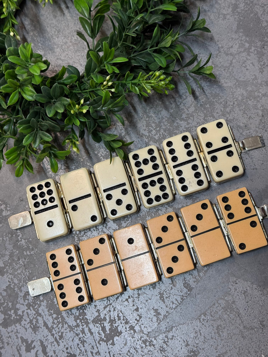 Two dominoes bracelets on a textured surface with greenery
