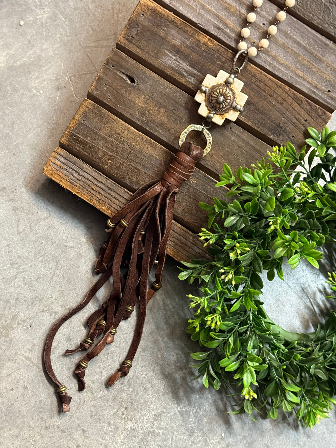 Necklace with tassel on a wooden surface with greenery