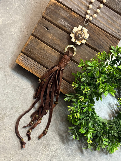 Necklace with tassel on a wooden surface with greenery