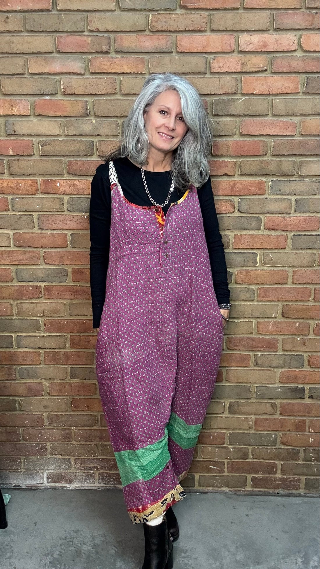 Person wearing a purple patterned overalls standing against a brick wall.