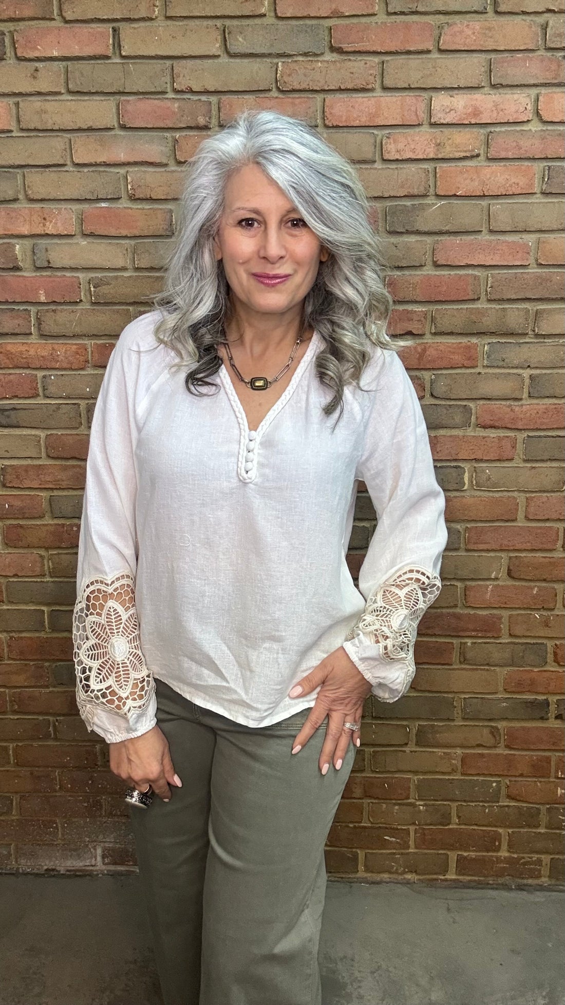 Woman wearing Linen Blend V-Neck Long Sleeve with Sage pants against brick wall.