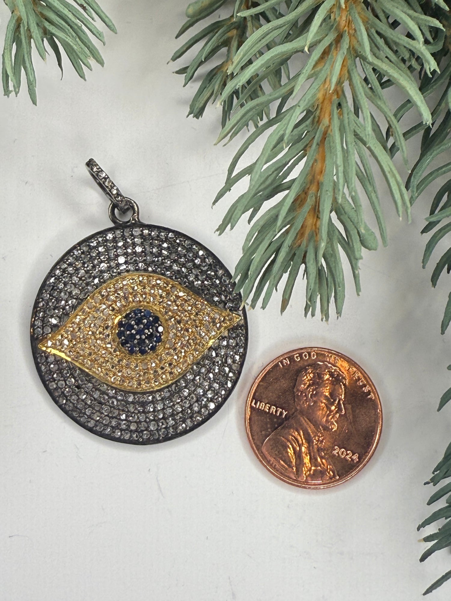 Gold and black pendant next to a penny on a white surface with greenery