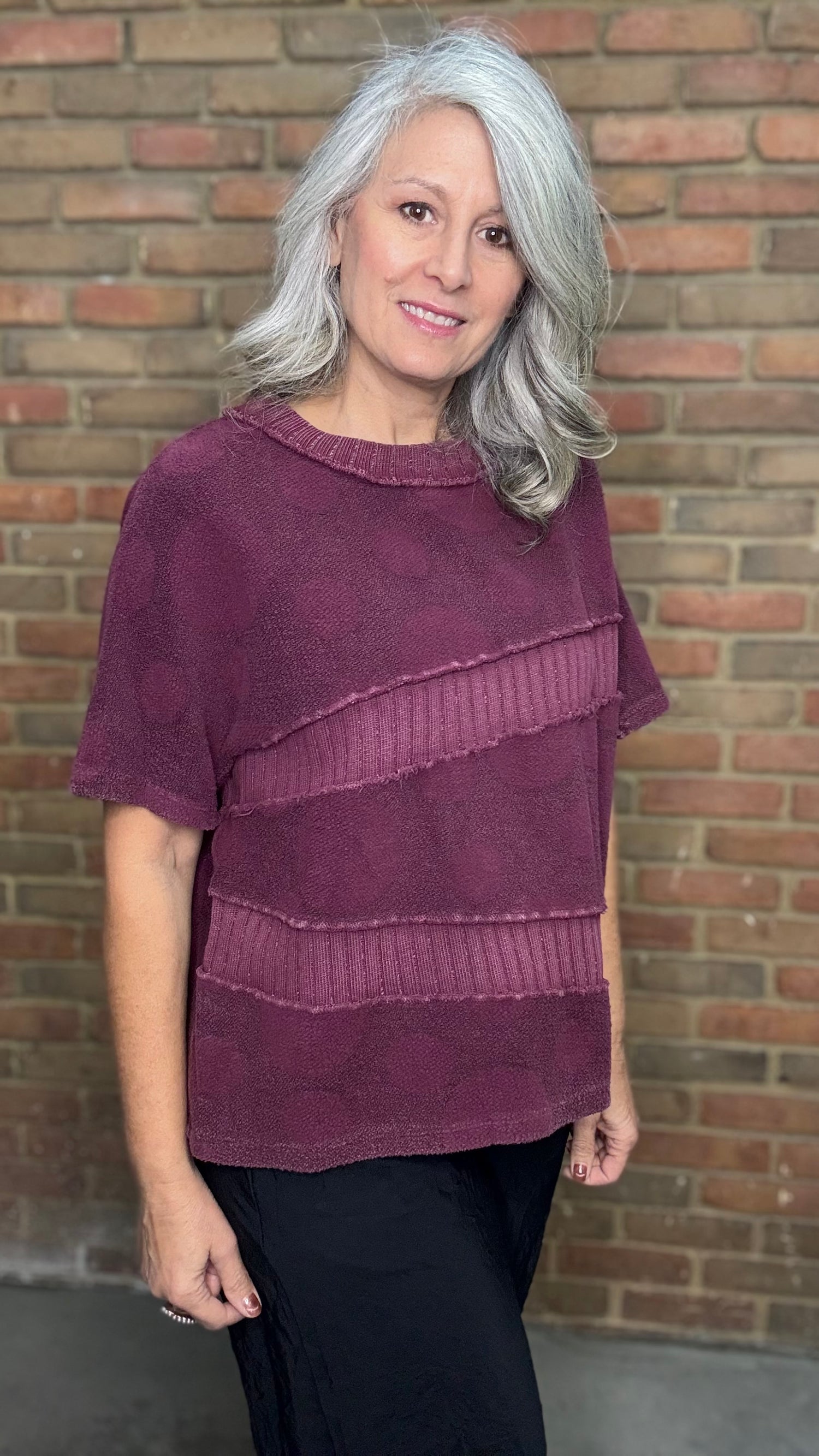 Woman wearing a purple layered sweater against a brick wall
