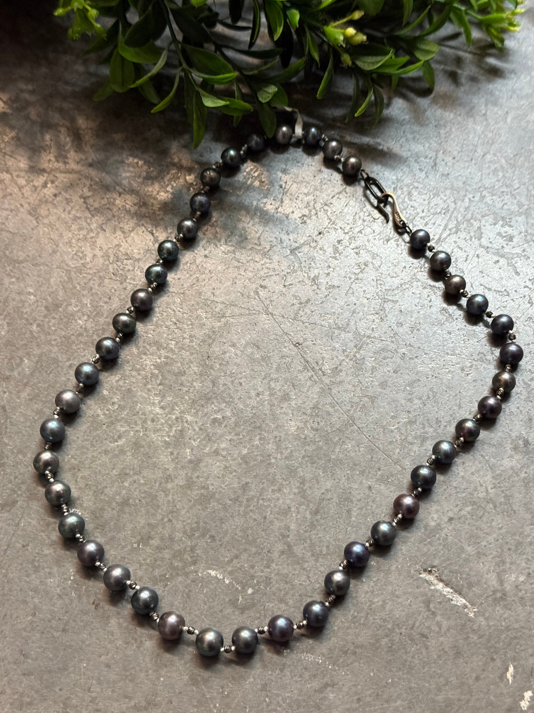 Black beaded necklace on a textured surface with greenery