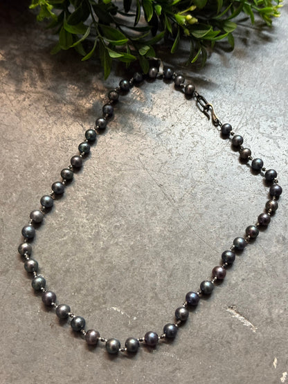 Black beaded necklace on a textured surface with greenery