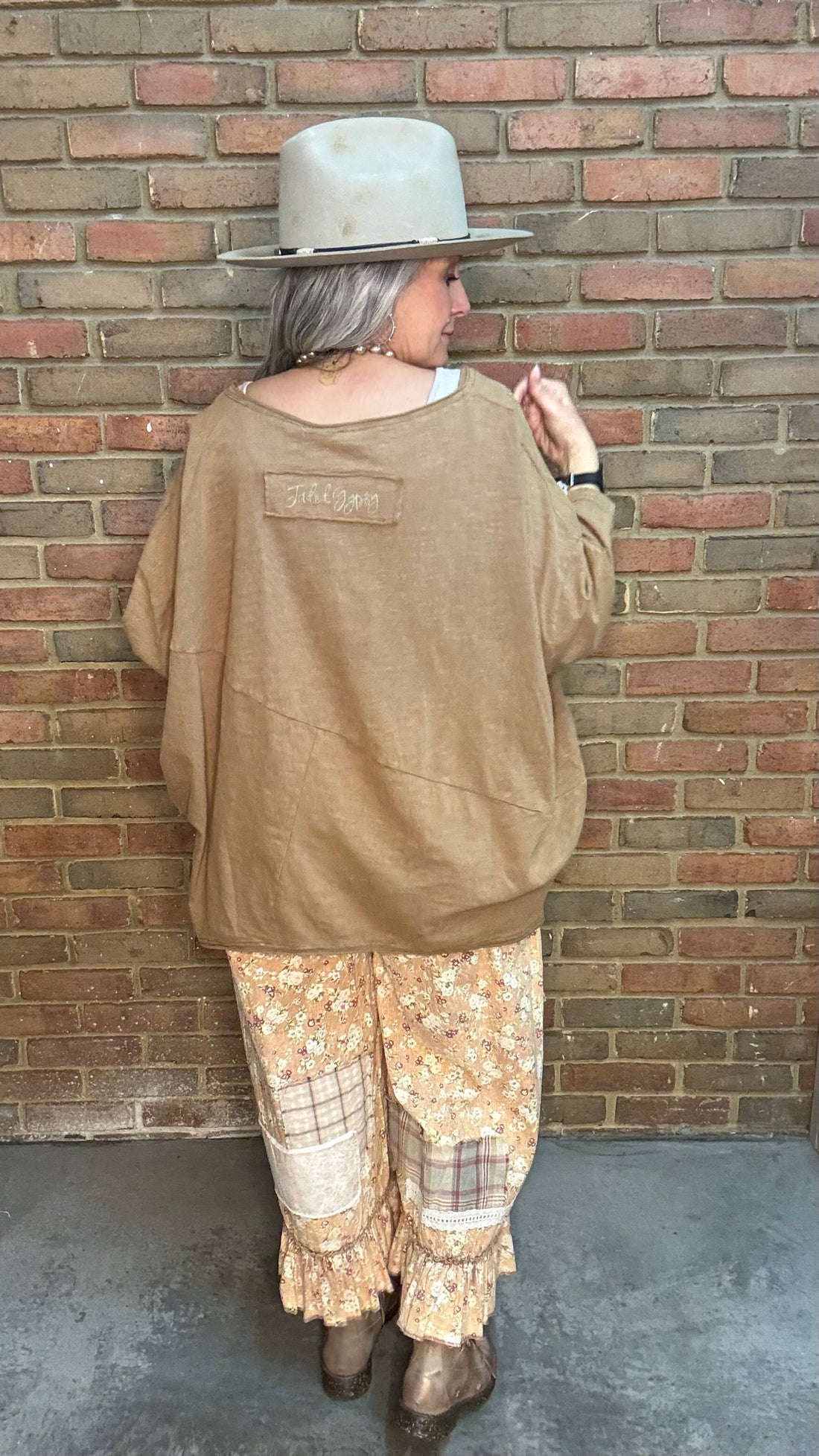 Woman wearing Be Free Top - Vintage Latte and patterned pants against a brick wall.
