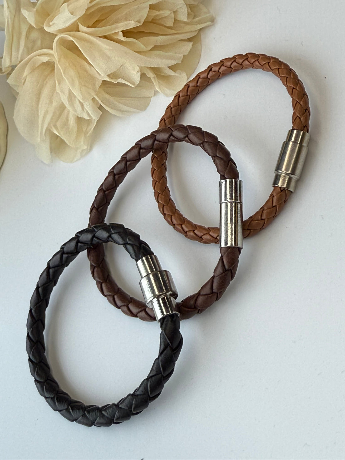 Three braided leather bracelets with metal clasps on a light background