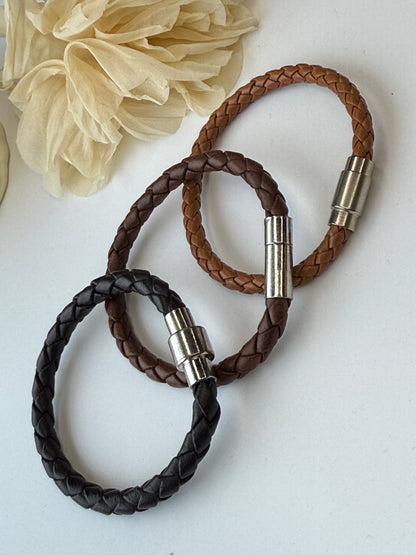 Three braided leather bracelets with metal clasps on a light background
