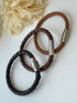 Three braided leather bracelets with metal clasps on a light background