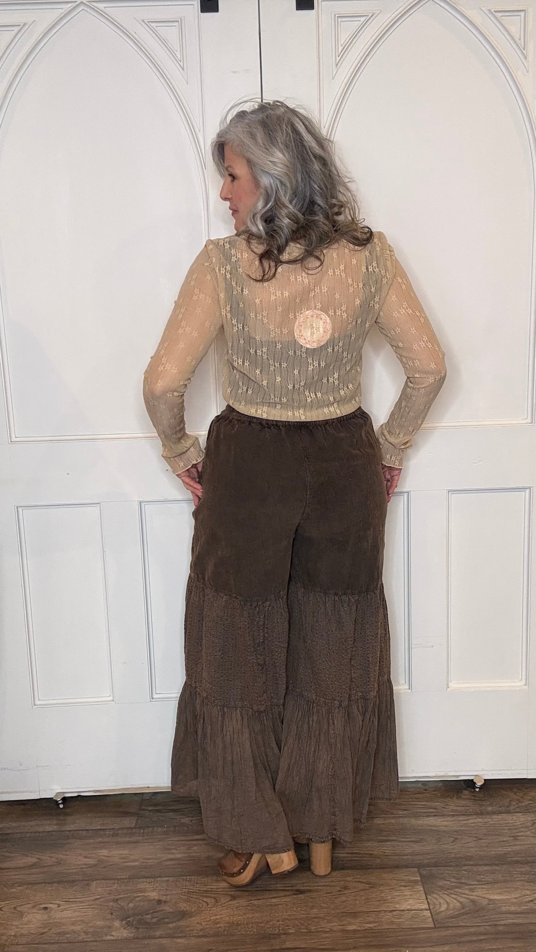 Woman wearing a beige lace top with Monarch Butterfly Necklace and Amber Boho Chic pants against a white paneled wall.