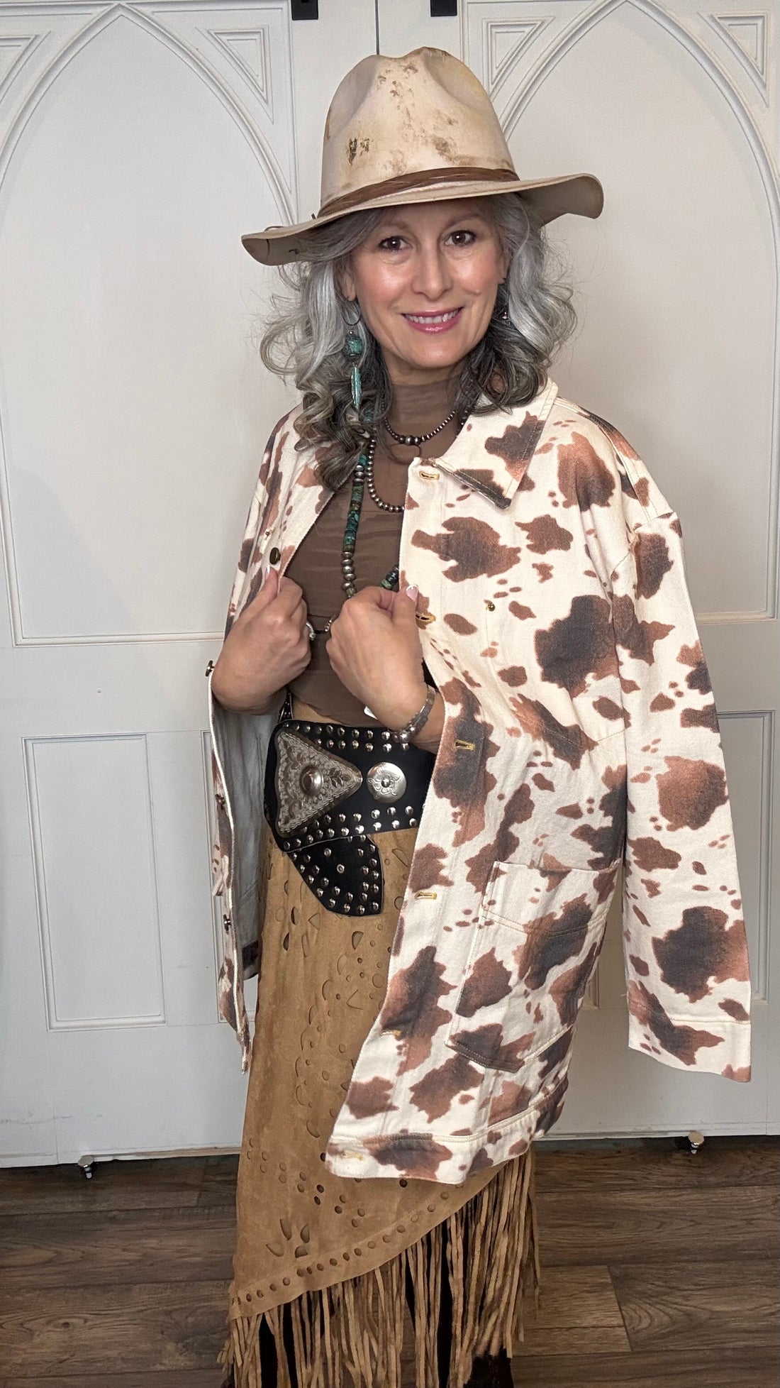 Woman wearing the Cow Print Denim Jacket, the Camel Faux Suede Fringe Skirt, topped the solid Mesh top in Brown and the Wide Triangle Buckle Belt.  Shoes are the Lane Plain Jane Boots, and she is wearing the Pop&