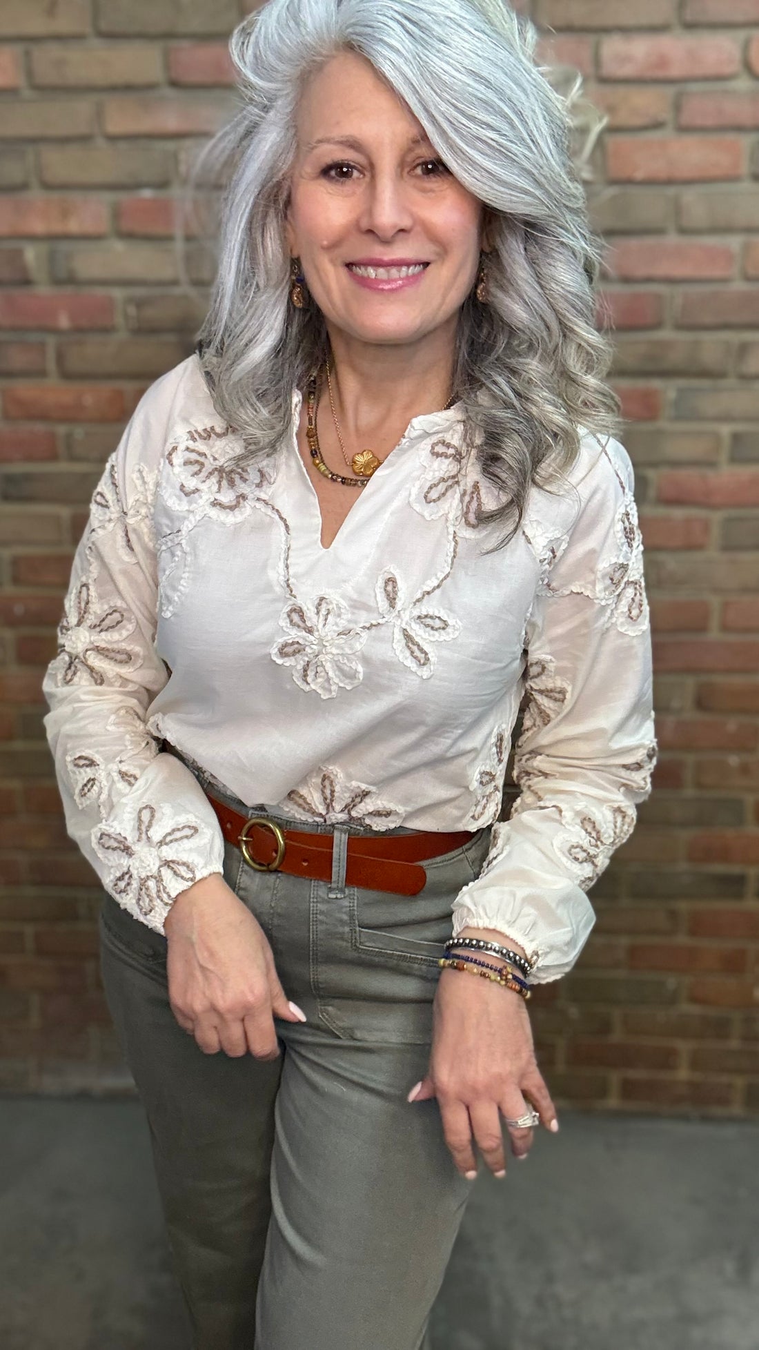 Woman wearing Embroidered Raglan Long Sleeve with Sage pants against brick wall.
