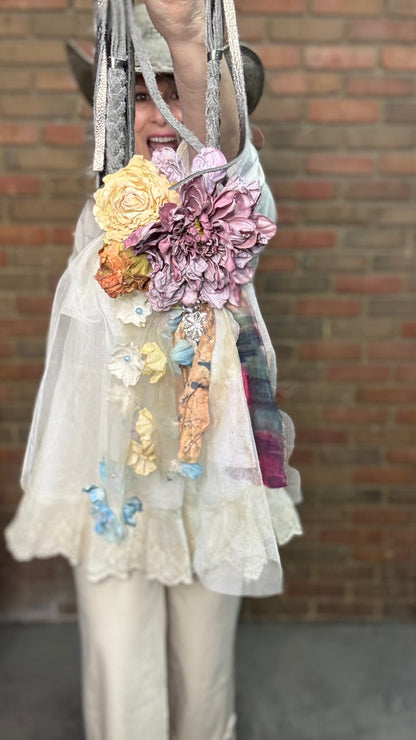 Person wearing a white outfit with Flower Garden Necklace and a cowboy hat against a brick wall.