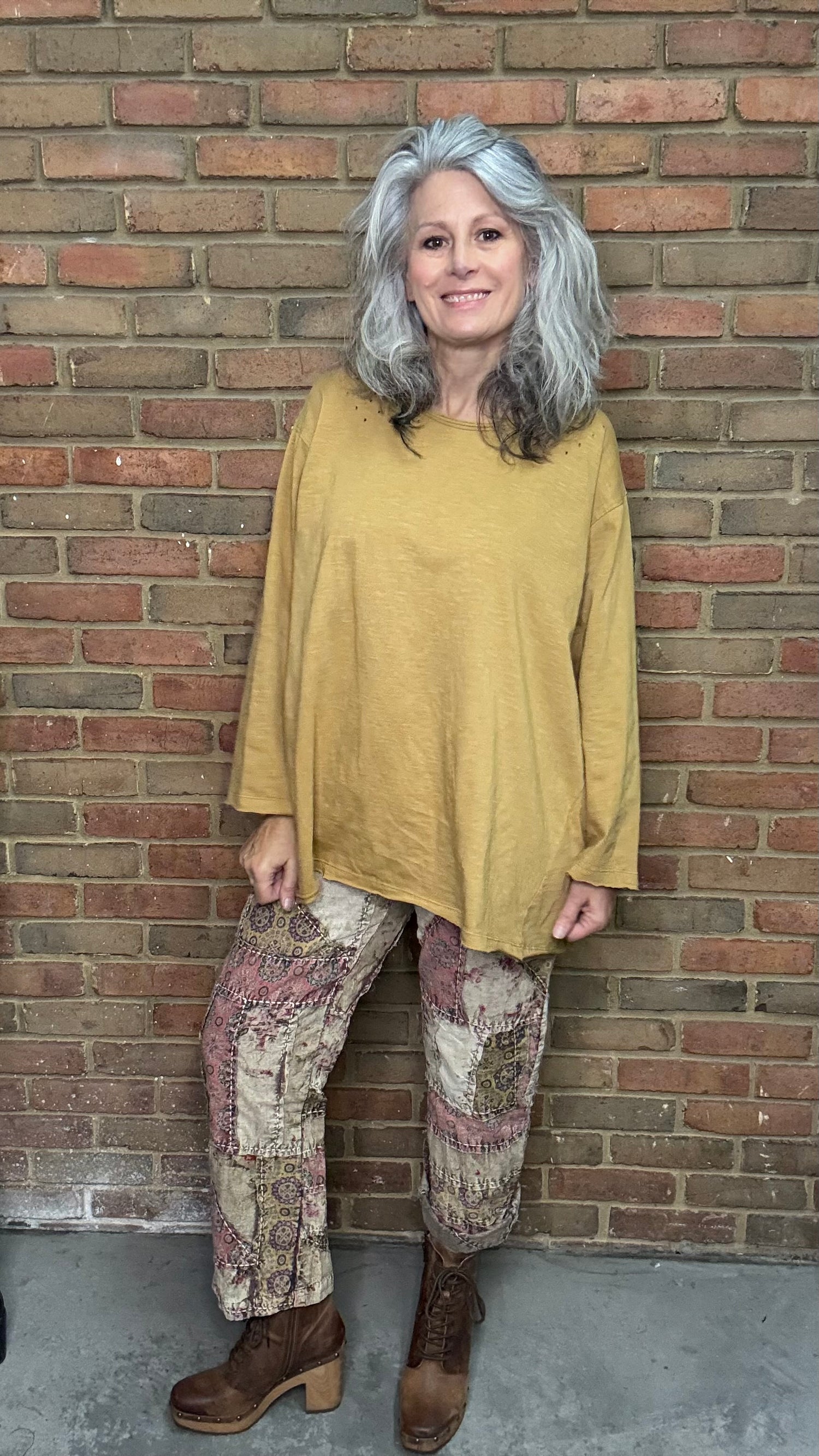 Woman wearing a mustard yellow top and patterned pants standing against a brick wall.