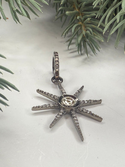 Star-shaped silver pendant with a central gemstone on a white background with green foliage.