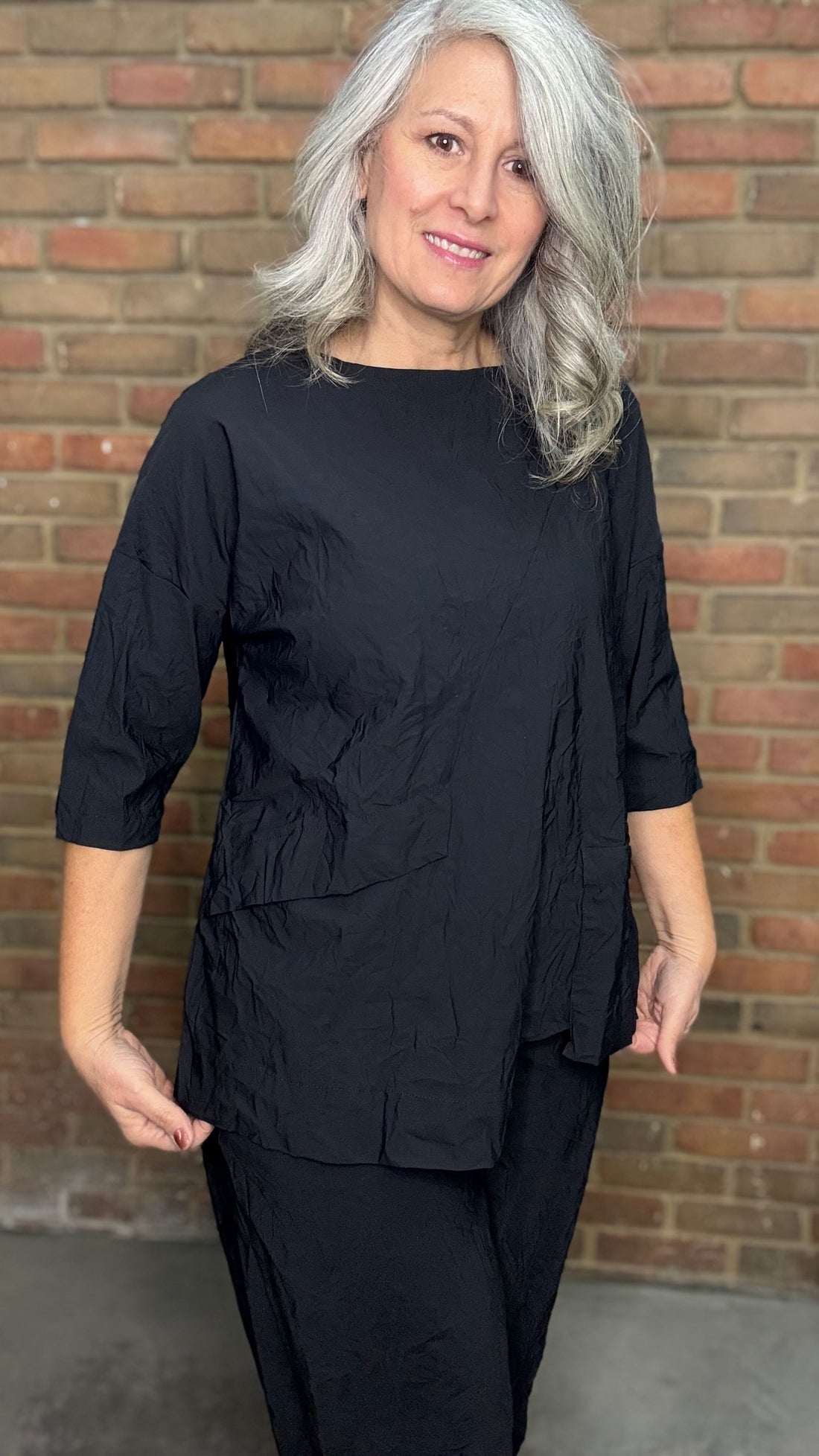 Woman wearing a black outfit standing in front of a brick wall