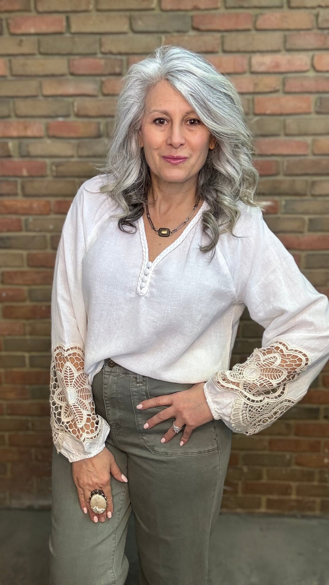 Woman wearing Linen Blend V-Neck Long Sleeve with Sage pants against brick wall.