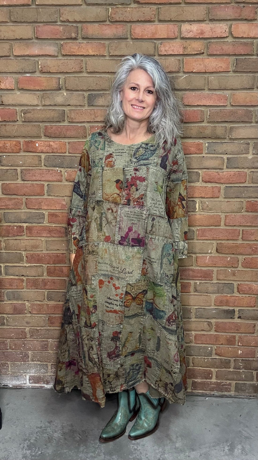Woman wearing a patterned dress and green boots standing against a brick wall.