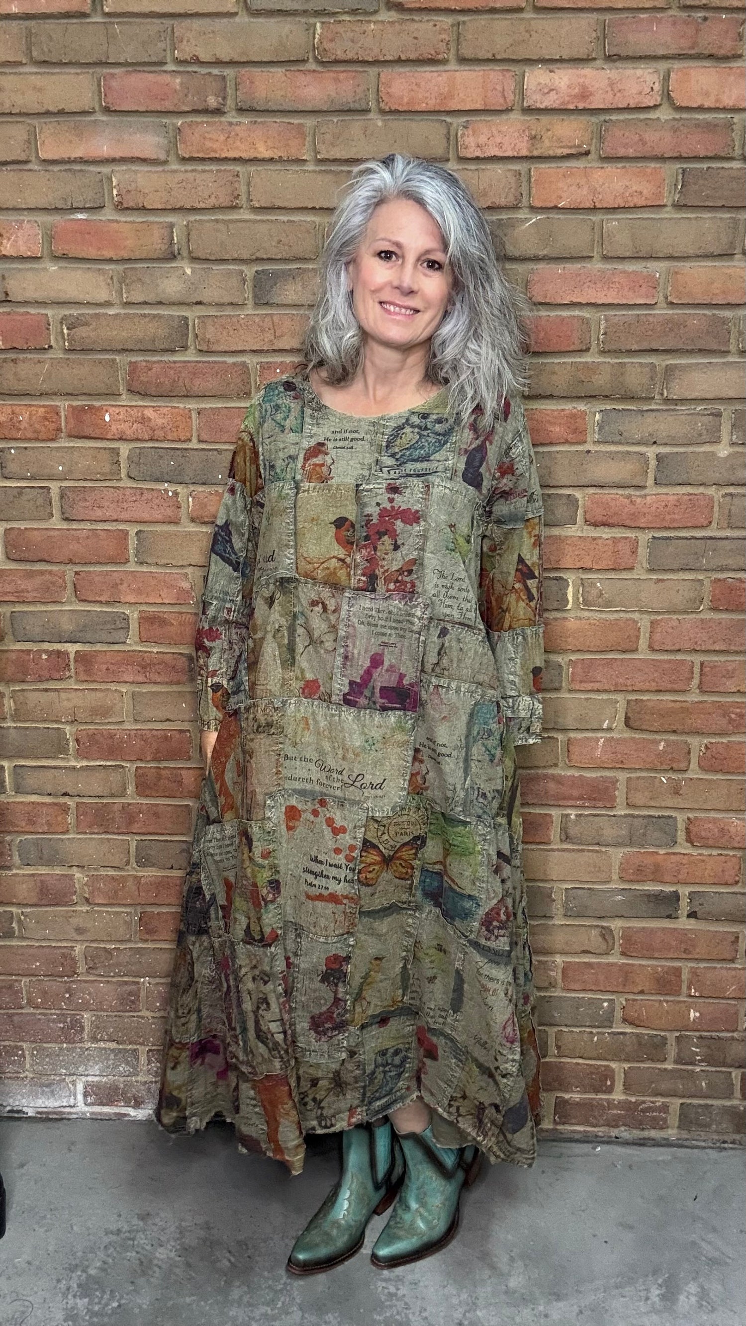 Woman wearing a patterned dress and green boots standing against a brick wall.