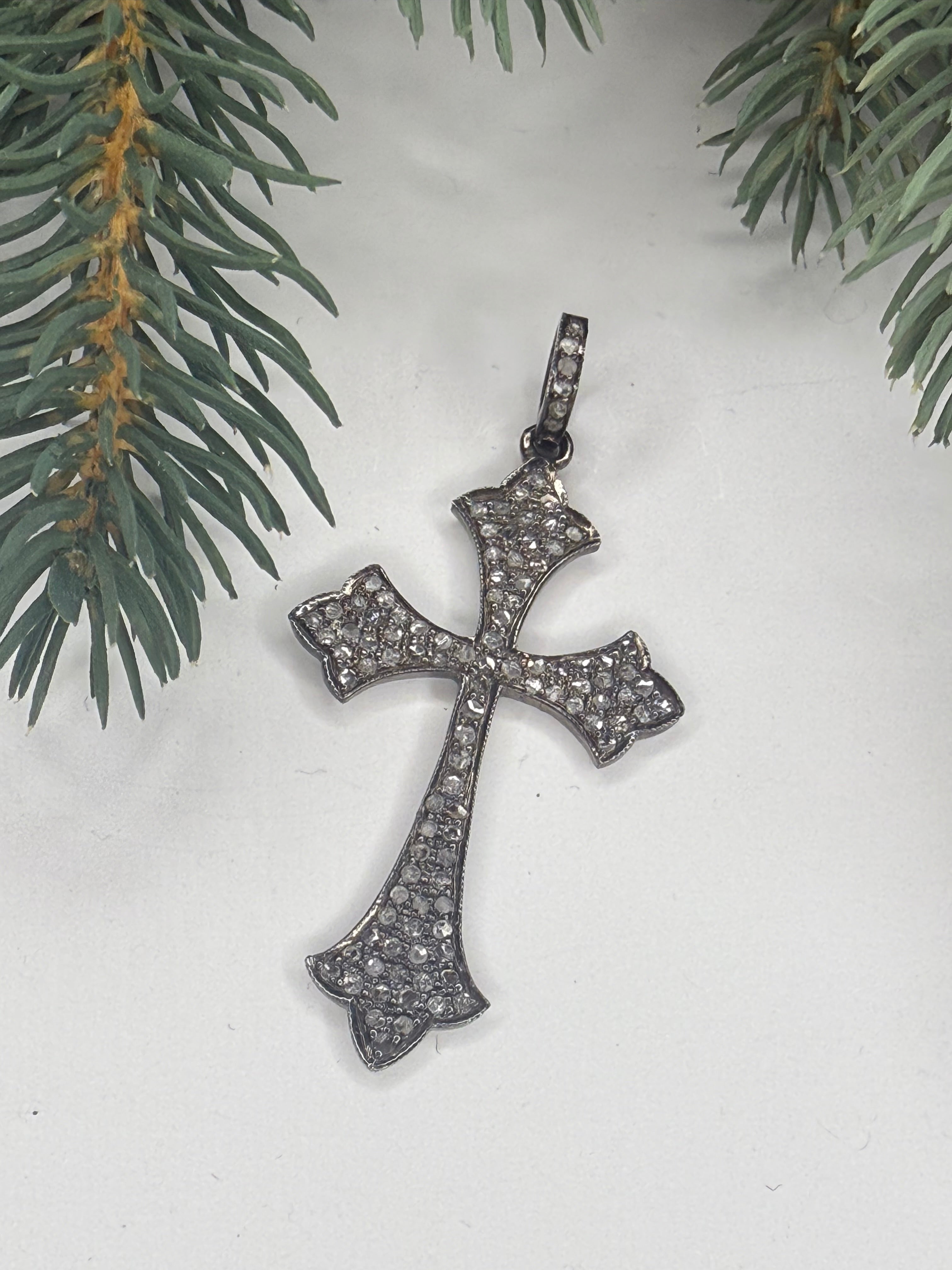 Silver cross pendant with pave diamonds on a light background with greenery