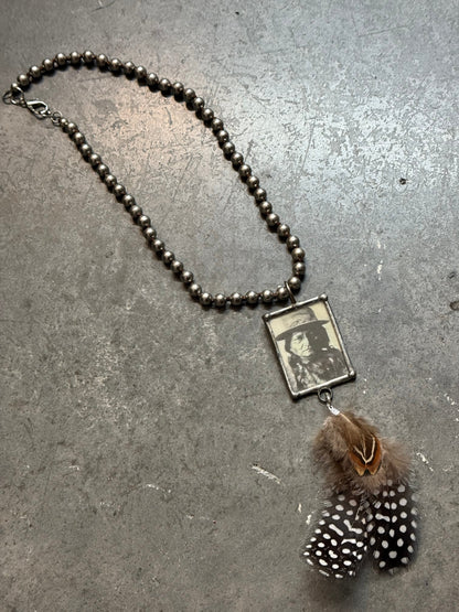 Necklace with feather charm and photo pendant on a textured surface