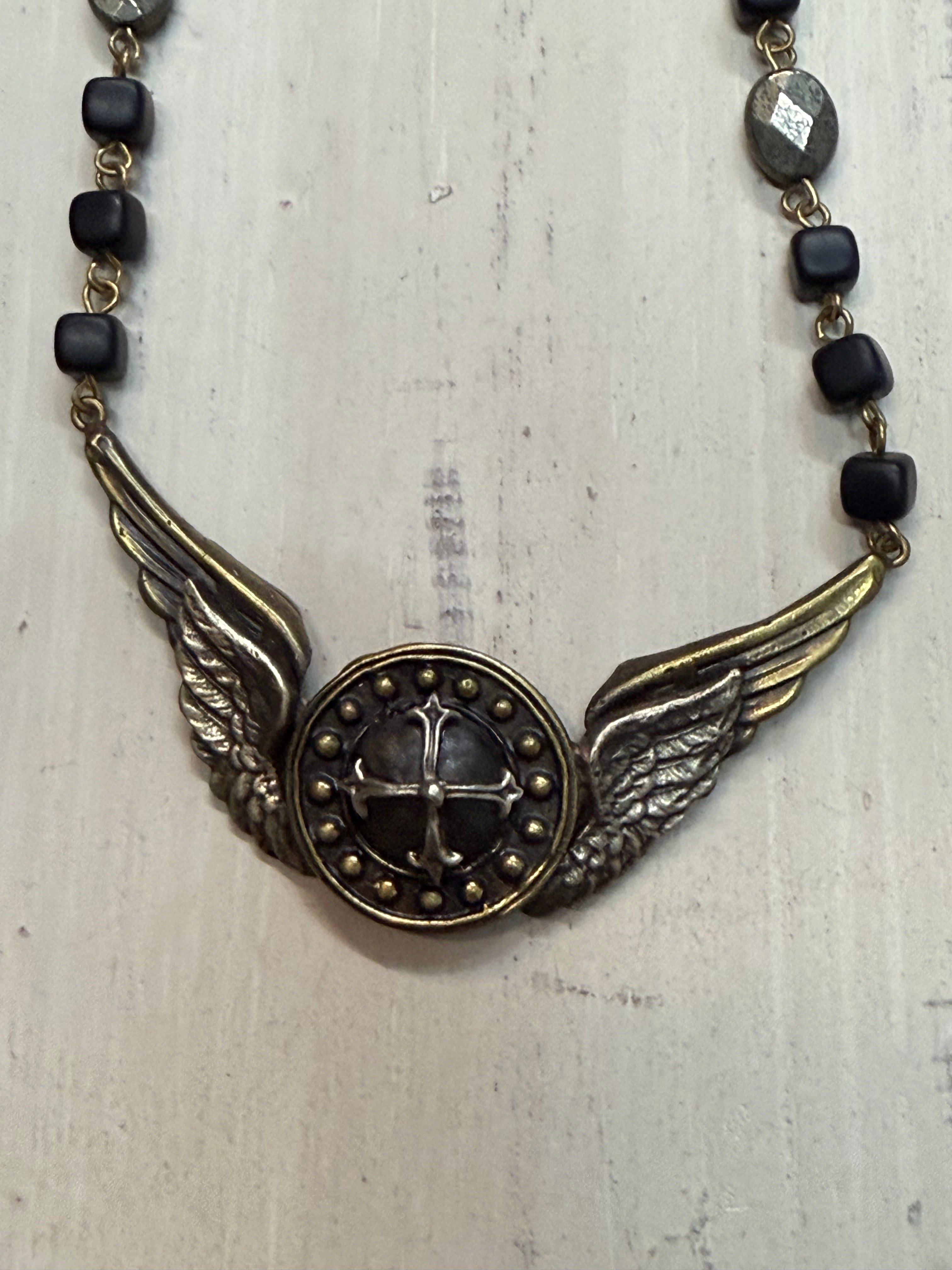 Necklace with winged pendant and black beads on a light wooden surface