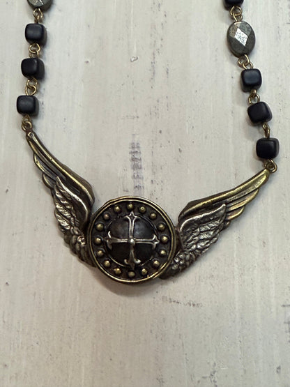 Necklace with winged pendant and black beads on a light wooden surface