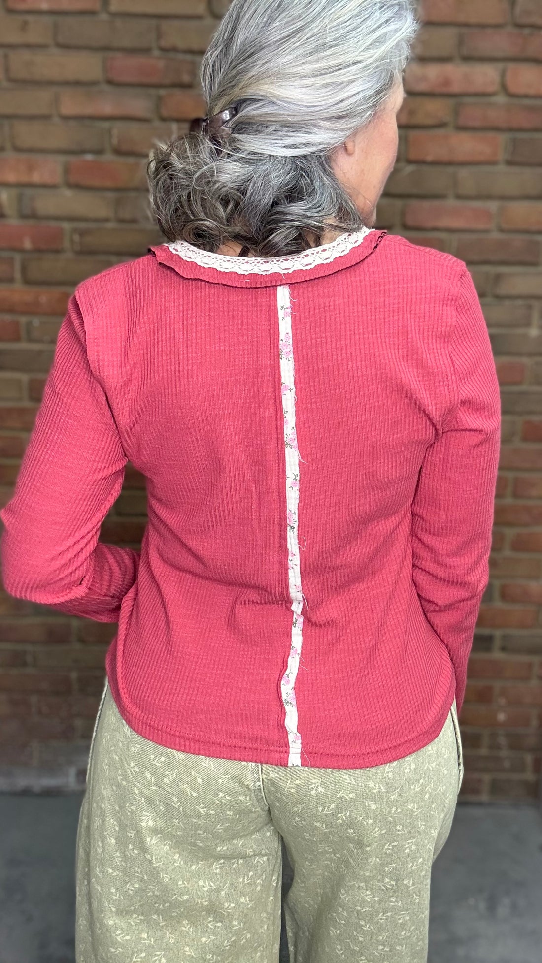 Person wearing the Raspberry Rose Ribbed Henley long-sleeve Top with the Floral Printed Barrel Pants against a brick wall.