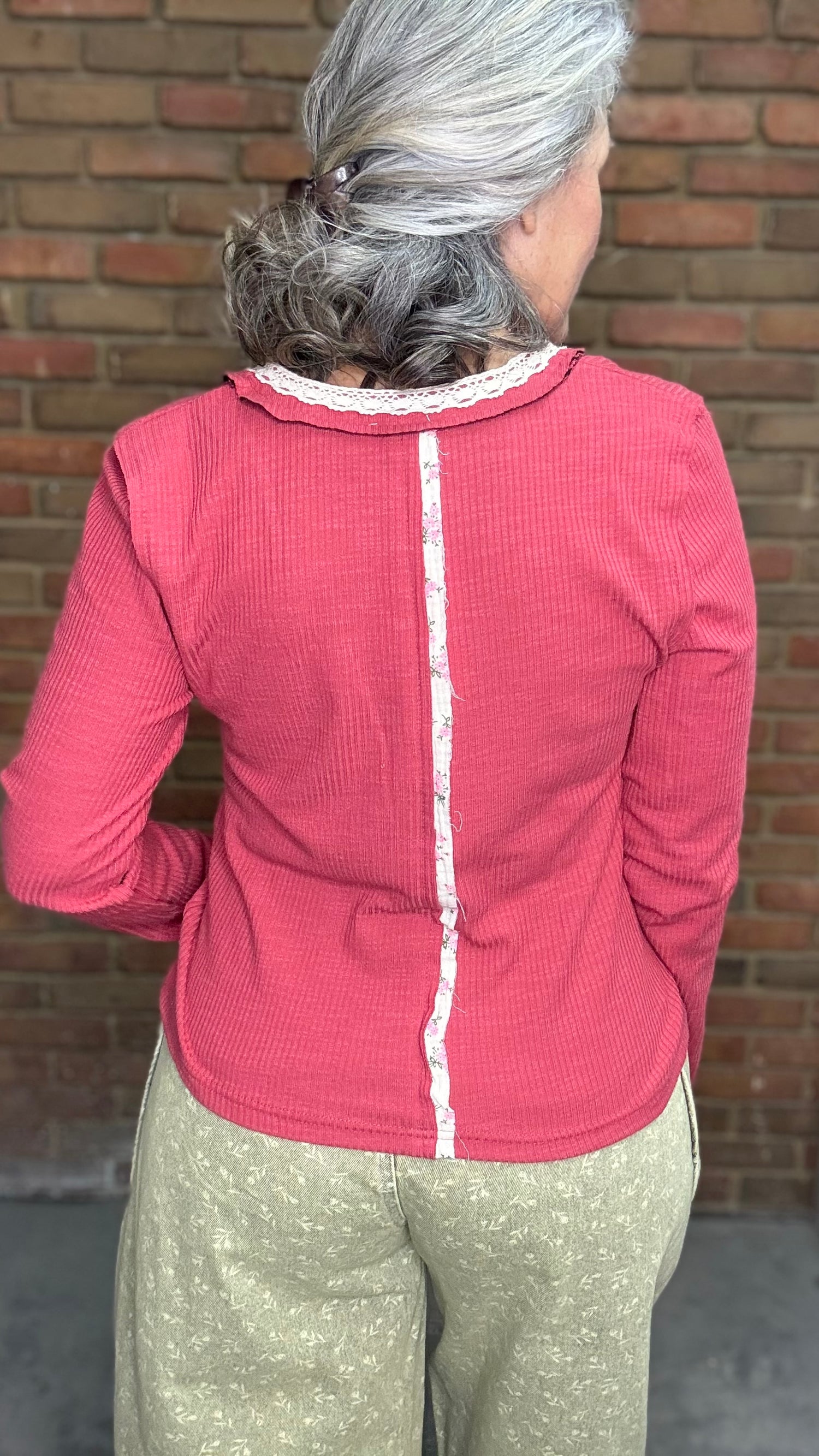Person wearing the Raspberry Rose Ribbed Henley long-sleeve Top with the Floral Printed Barrel Pants against a brick wall.