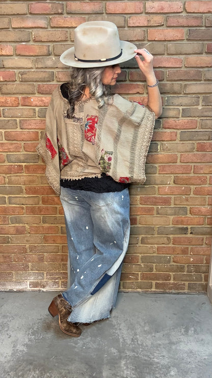 Woman wearing Garden Drift Top with a hat, jeans, and belt against a brick wall.