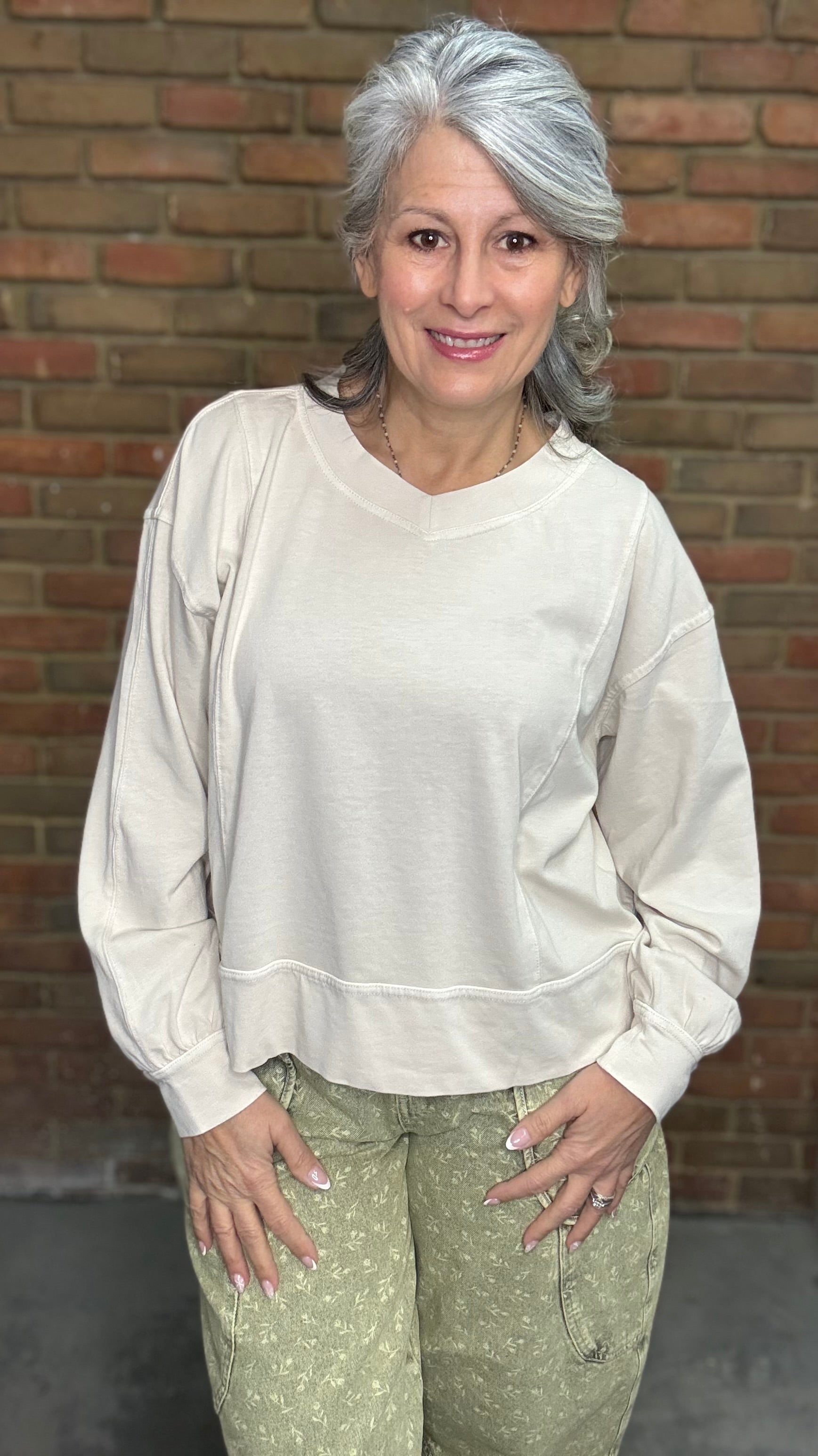 Woman standing against a brick wall wearing the Taupe Long Sleeve Top and Floral Printed Barrel Pants.