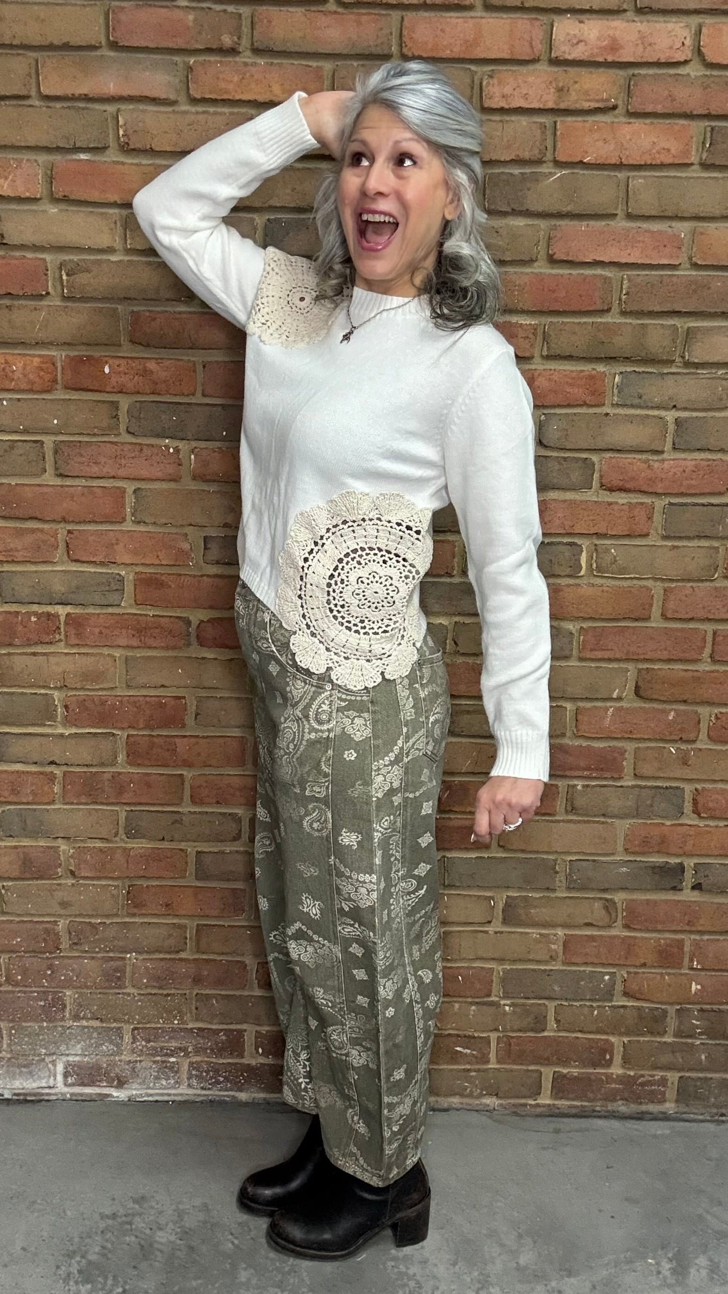 Woman wearing the Crochet Detail Cropped Sweater and the Paisley Print Jean standing against a brick wall.