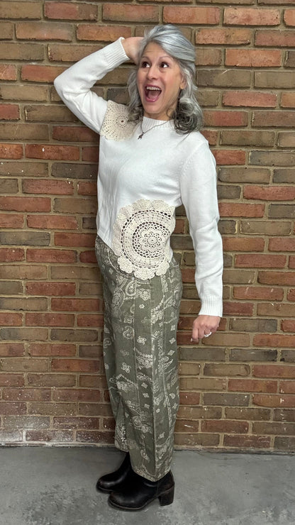 Woman wearing the Crochet Detail Cropped Sweater and the Paisley Print Jean standing against a brick wall.