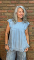 Woman wearing a light blue top and jeans standing against a brick wall.