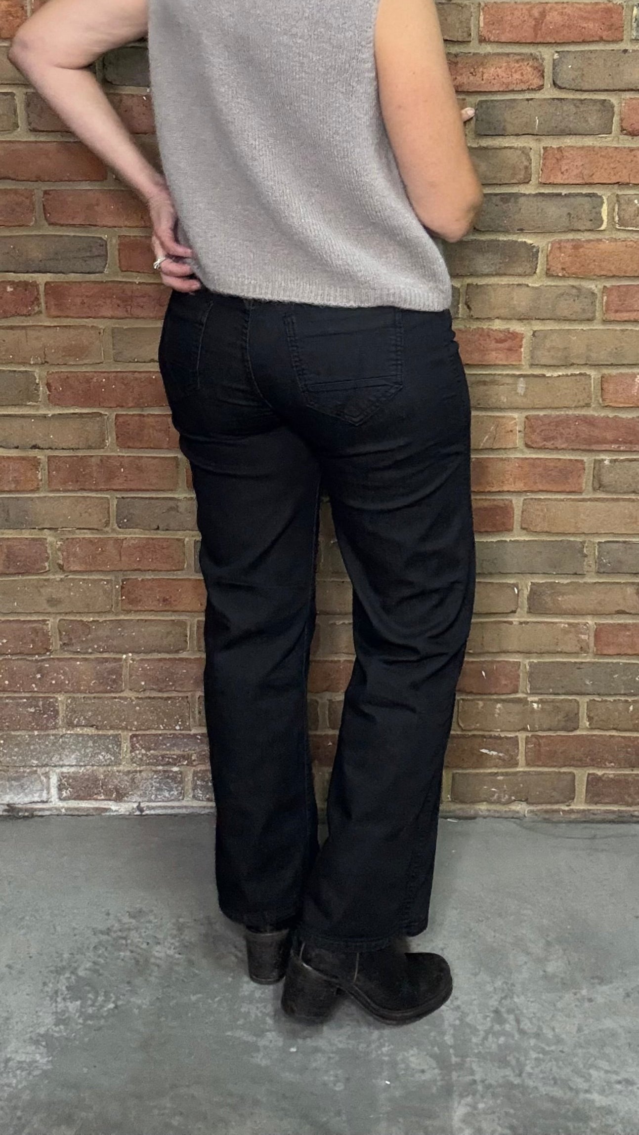Person wearing a gray sleeveless top and black pants against a brick wall.
