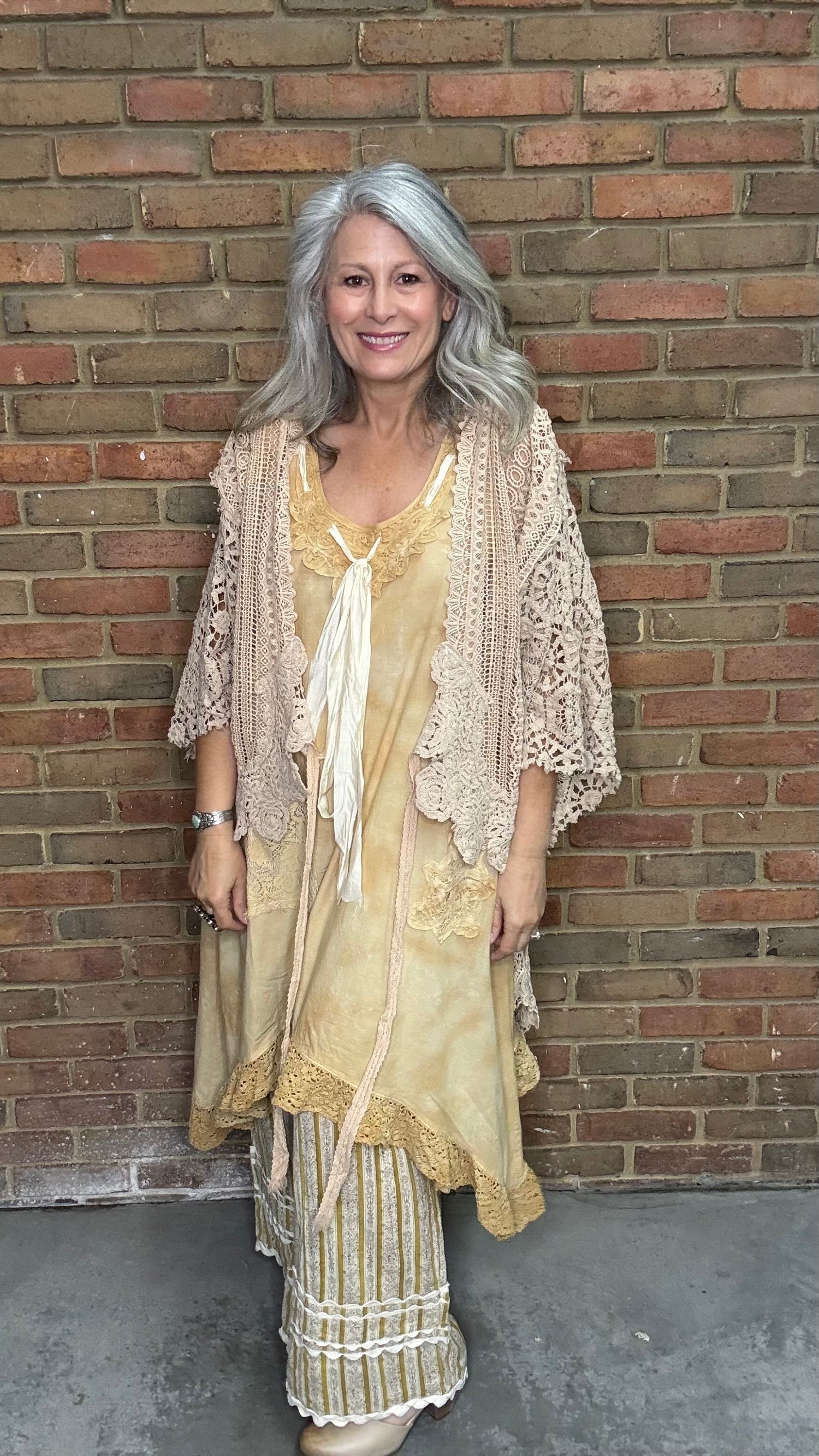 Woman wearing the crochet Forever Timeless Split Tails Jacket over the Wandering Spirit Dress with striped pants standing against a brick wall.