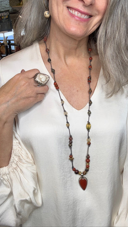 Woman wearing a white top and a long necklace with a ring, indoors.