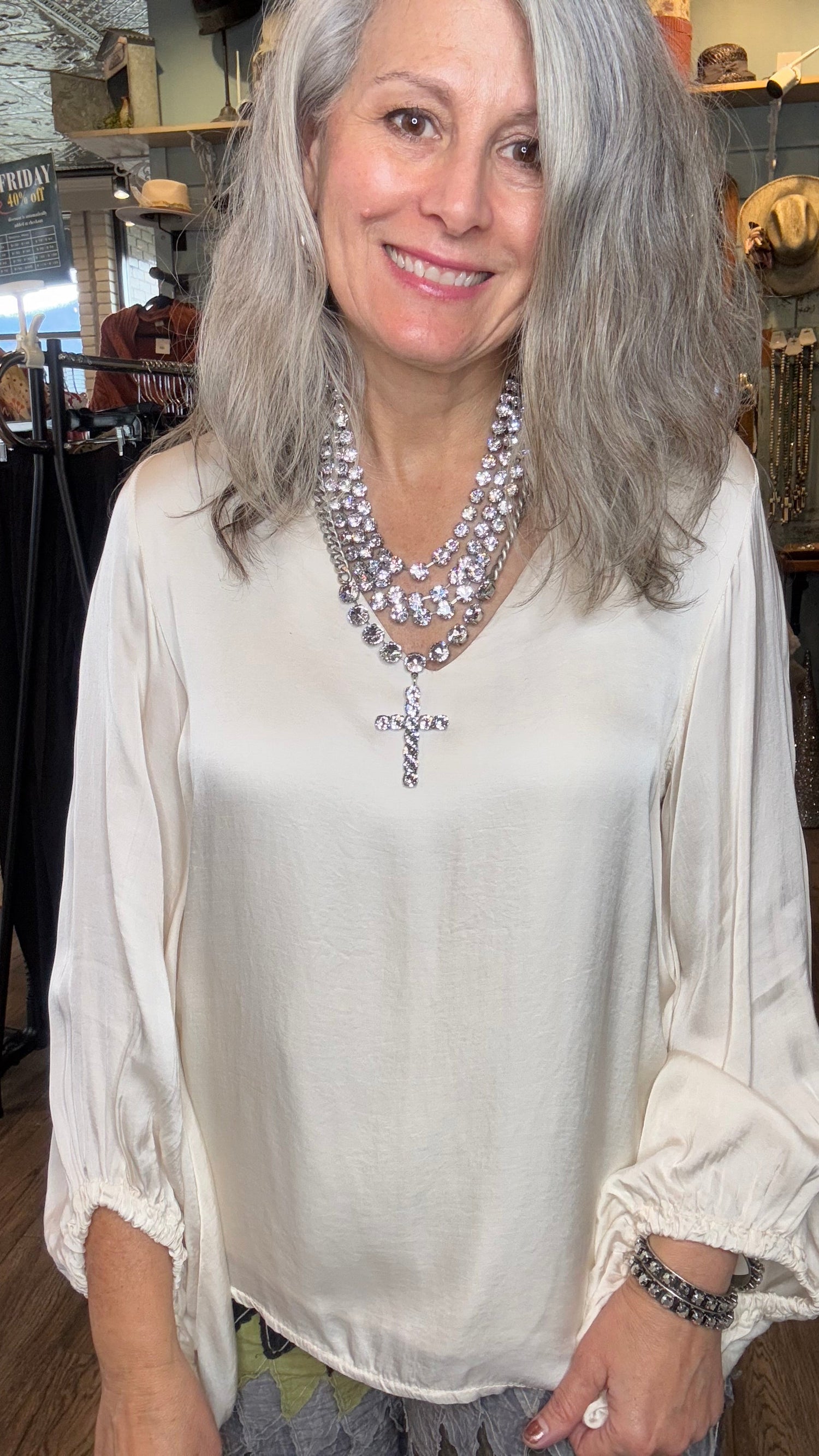 Woman wearing a white blouse with a cross design and pearl necklace indoors.