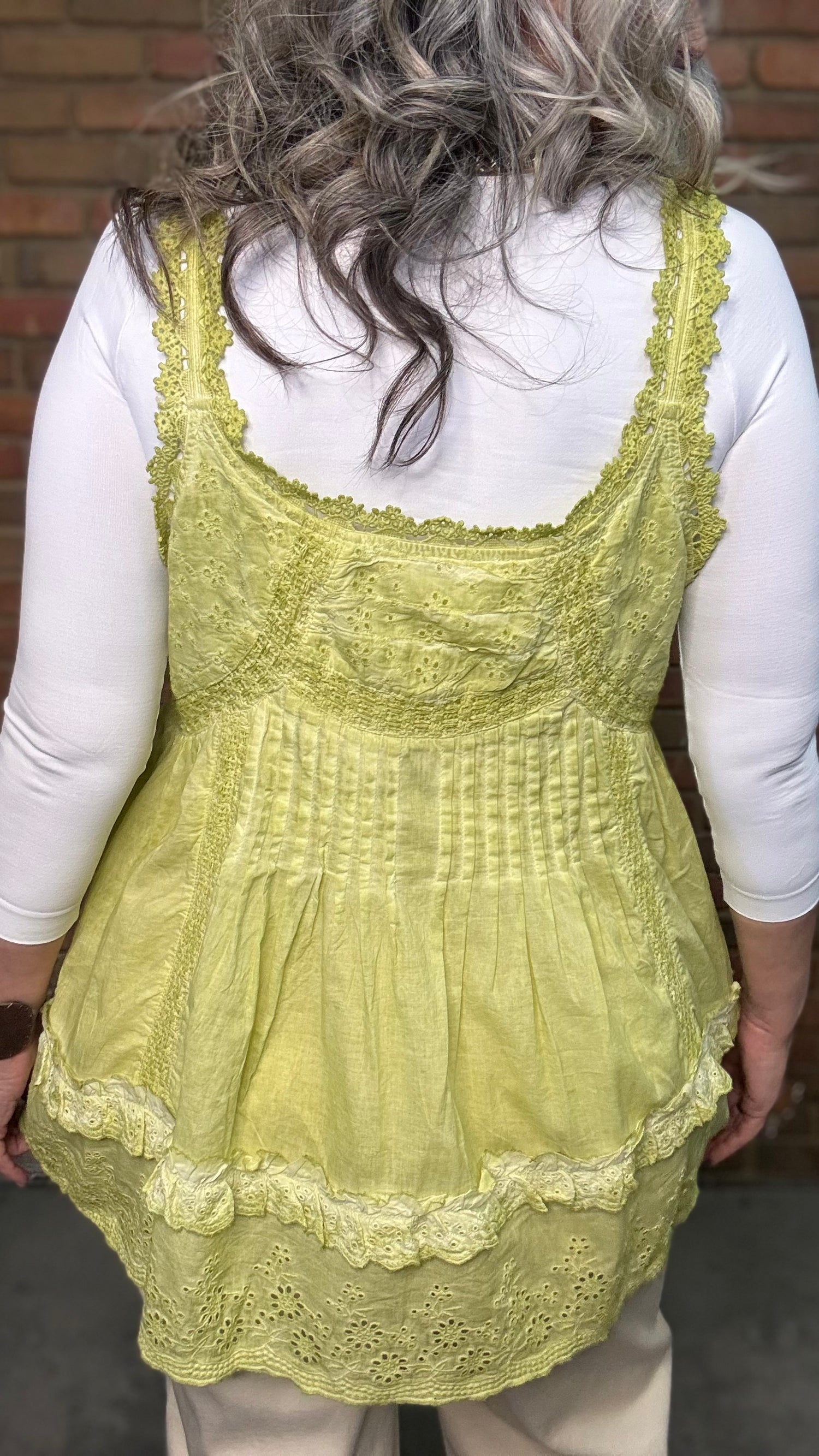Woman wearing Eyelet Lace Tank over a white shirt, standing against a brick wall.