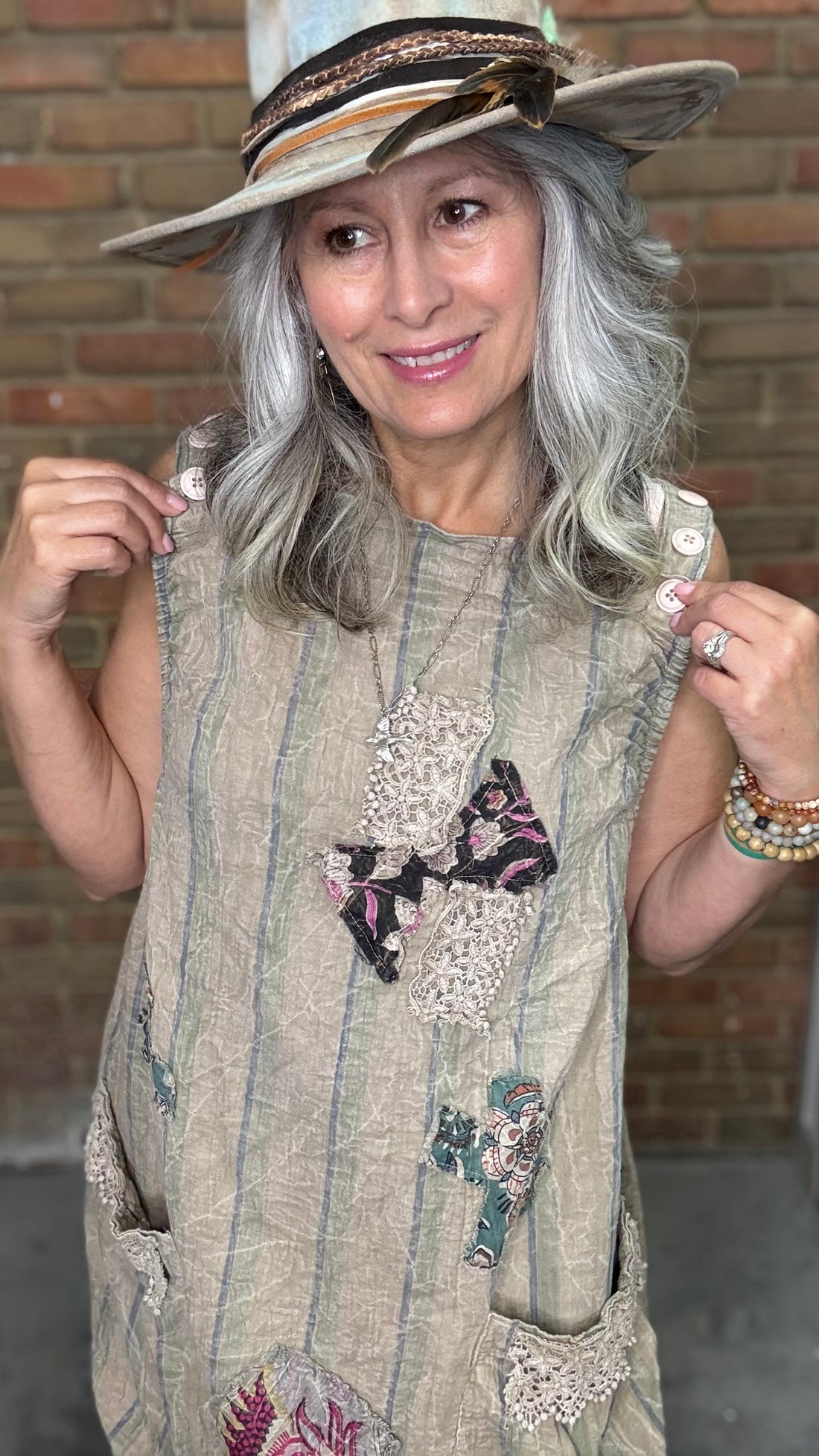 Woman wearing a patterned dress with butterfly designs against a brick wall.