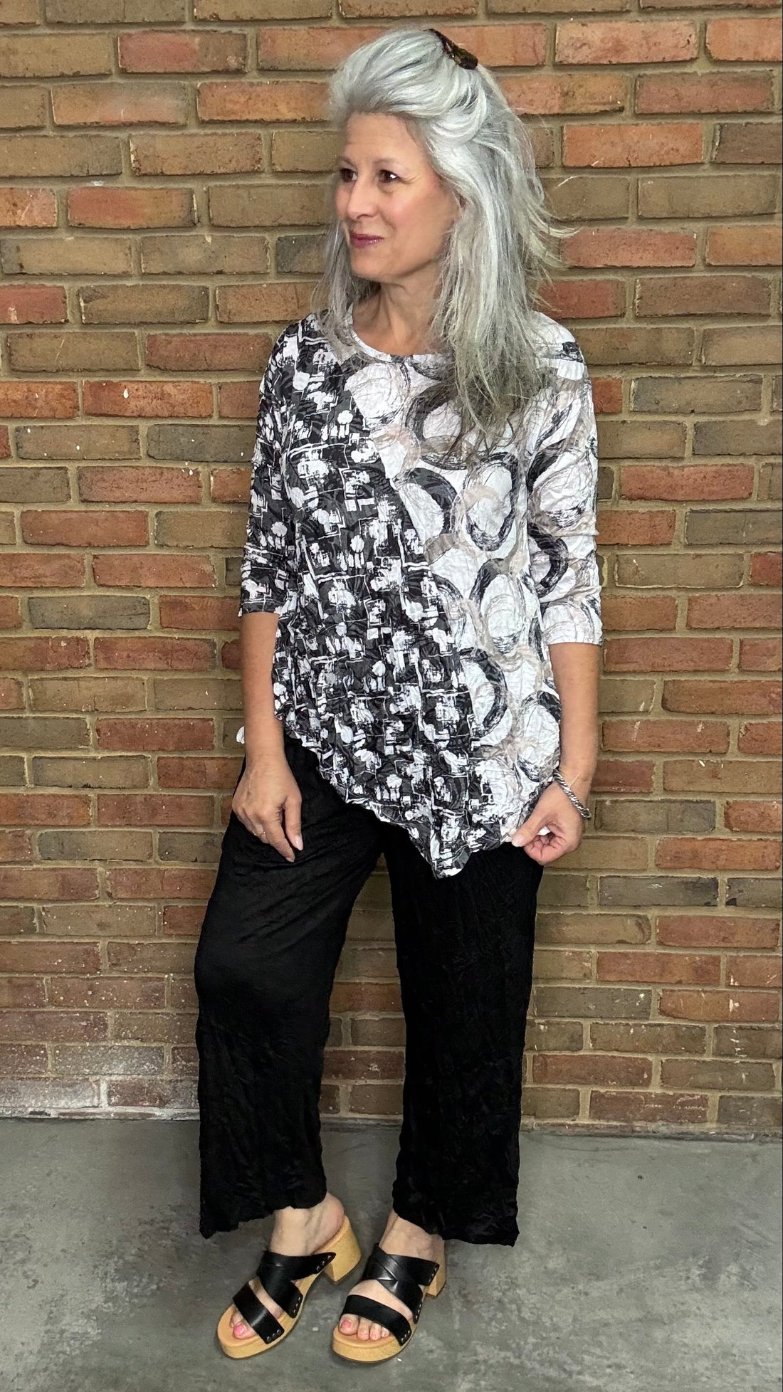 Woman wearing a patterned top and Black Capri Straight Leg Pant standing against a brick wall.