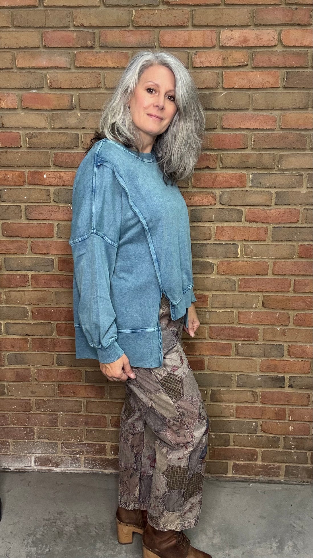 Woman standing against a brick wall wearing a blue jacket and patterned skirt.